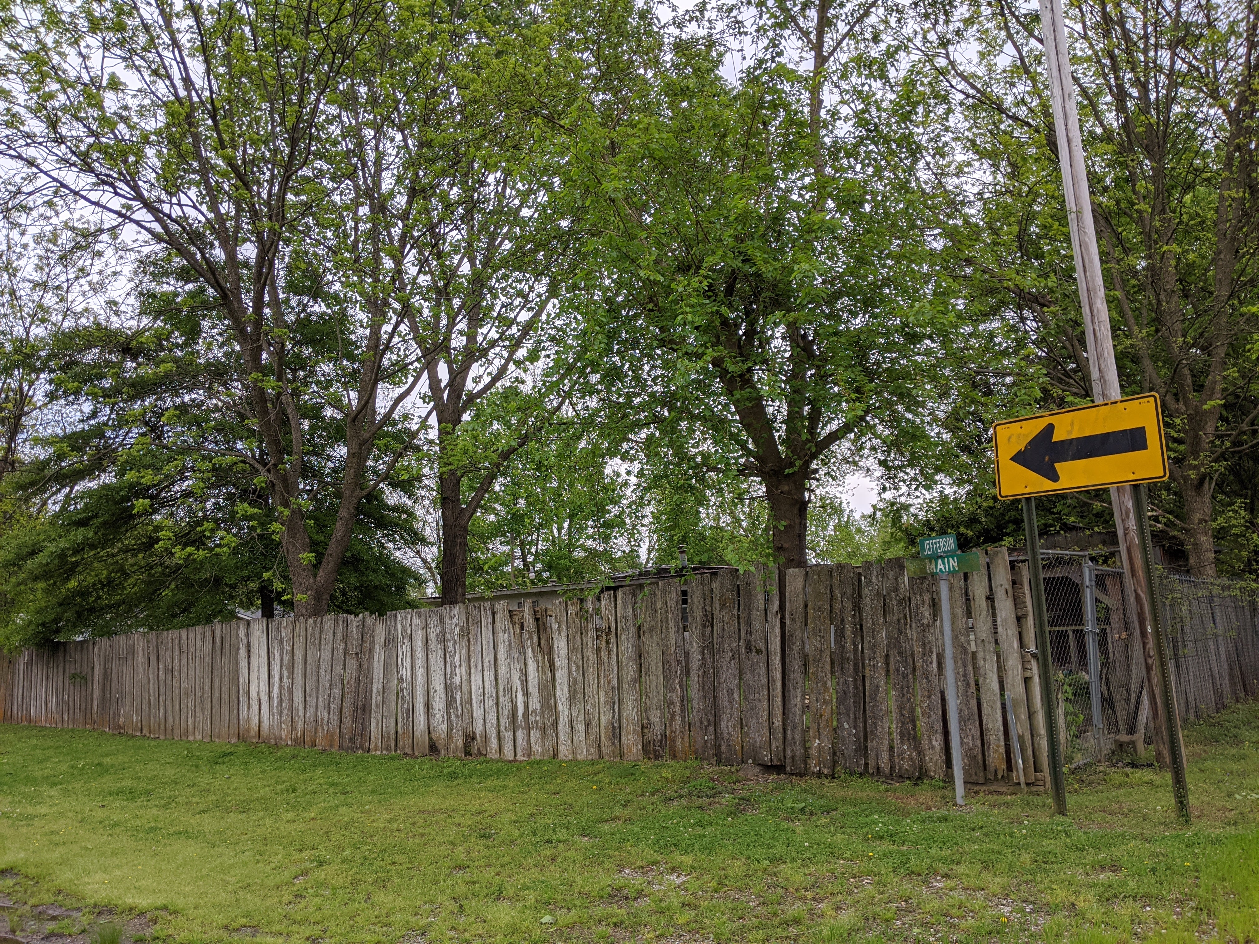 a weathered wooden fence with the street sign for Jefferson and Main at its corner and trees on the lot in the background
